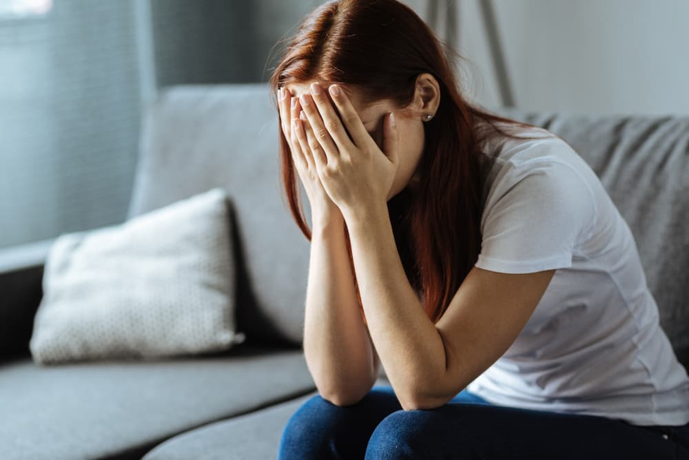 Distressed young woman hiding her face in her hands.