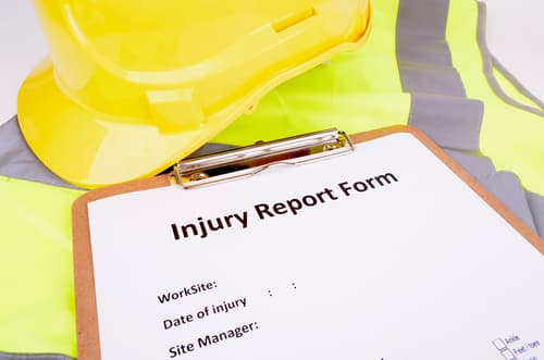 clipboard with and injury report form on table next to construction vest and helmet