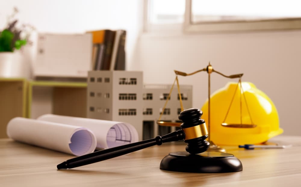 A judge's gavel rests on building blueprint plans with a yellow safety helmet in the background, symbolizing law related to building construction and engineering.






