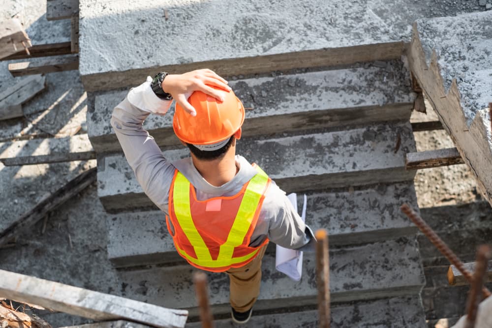 A male architect or engineer wearing a hard hat, adjusting it as he walks up the stairs at a new building construction site.