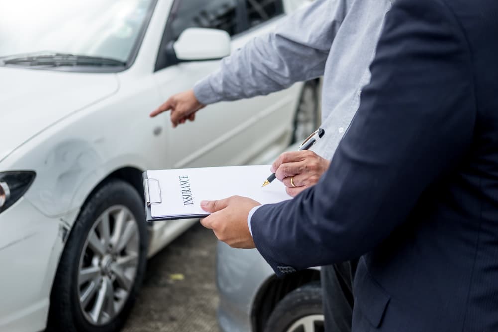 The image of an insurance agent examining a car after an accident and writing on a clipboard during the claims process.