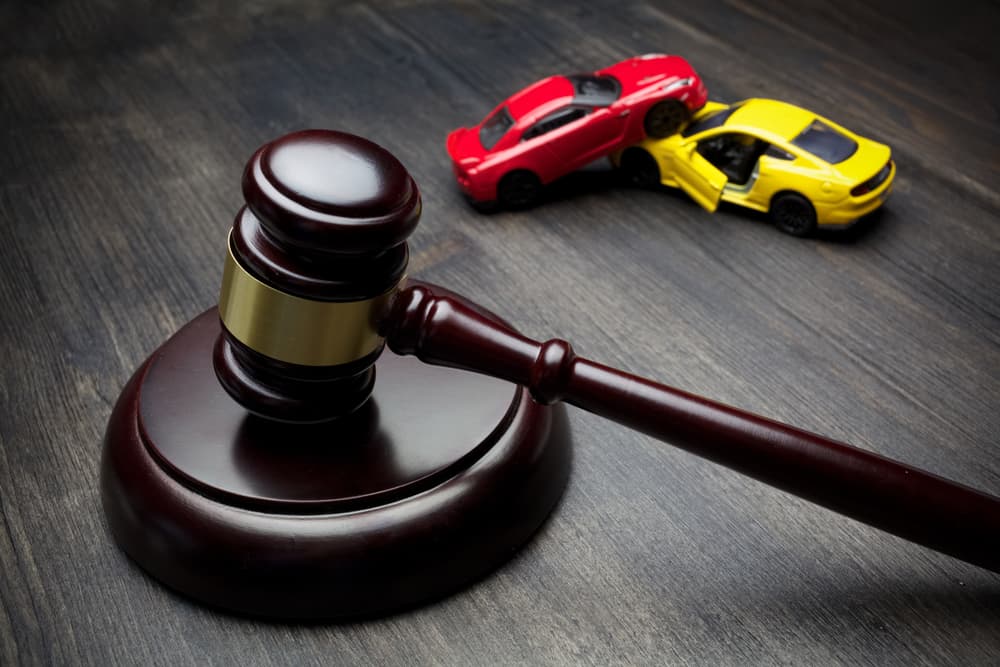 A judge's gavel next to two cars that have collided in an accident.






