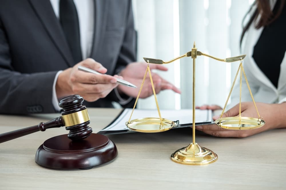 A professional male lawyer or legal counselor is seated at a desk, engaged in a negotiation discussion with a client. 