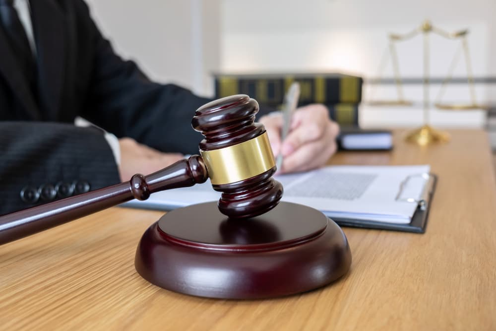 Legal advice and justice concept: A male lawyer or notary reviewing important case documents with a wooden gavel and balance scale on the courtroom table.