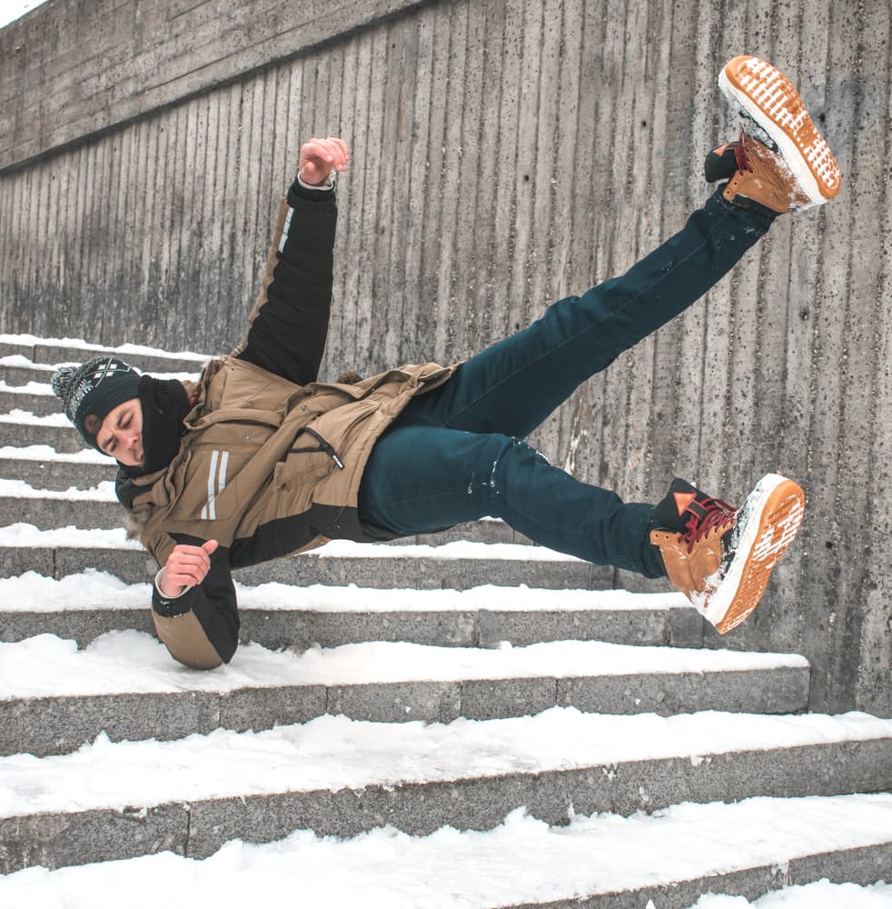 Man slipping and falling down stairs in winter, surrounded by snow and ice, capturing the concept of hazardous winter conditions and personal injury.