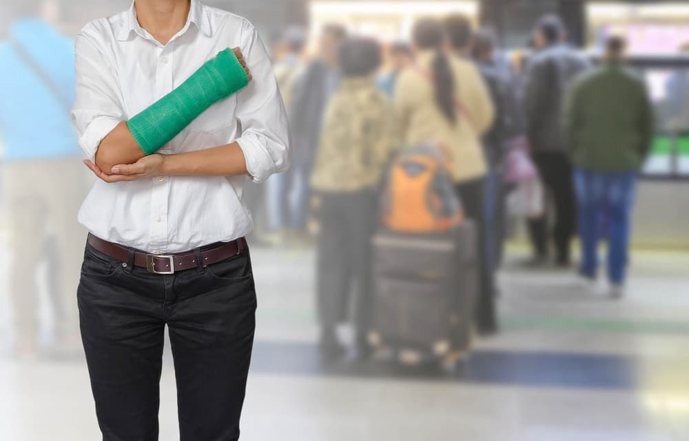 Injured woman with a green cast on her hand and arm, standing in a subway station with a motion-blurred background, symbolizing a body injury concept.







