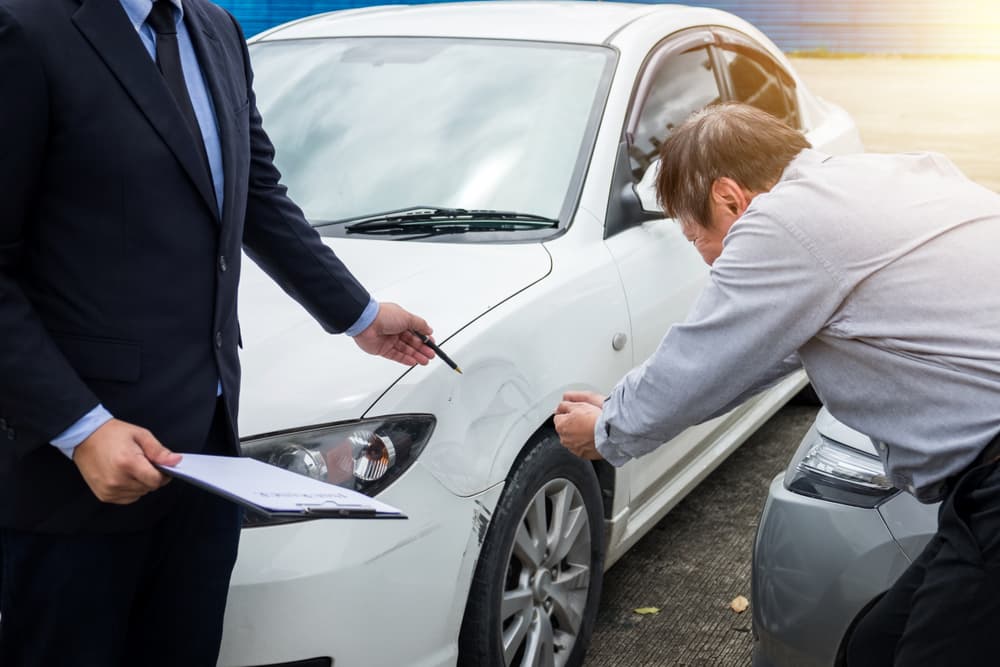 An insurance agent inspects a damaged car and fills out a claim report after a traffic accident, representing the insurance and claims process.







