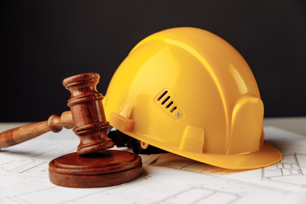 A close-up of a wooden gavel alongside a yellow safety helmet, symbolizing construction law.







