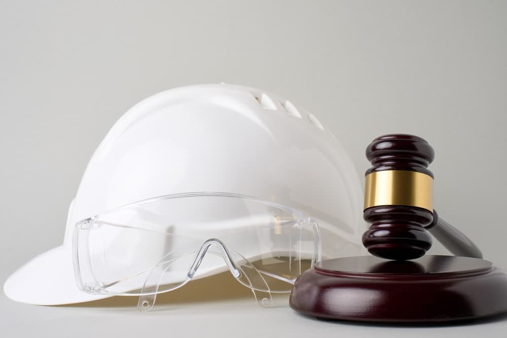 Labor laws and employment regulations concept: A safety hard hat and judge's gavel placed on a gray background.